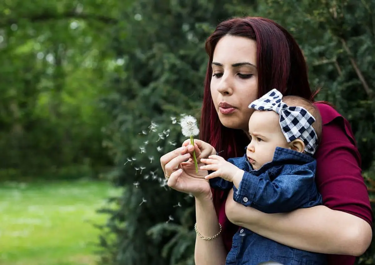 woman holding a baby and blowing on a dandelion